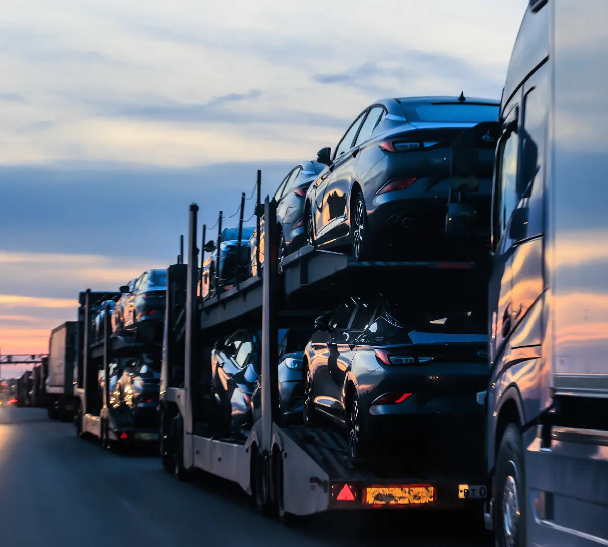 A car carrier truck loaded with black vehicles at sunset.