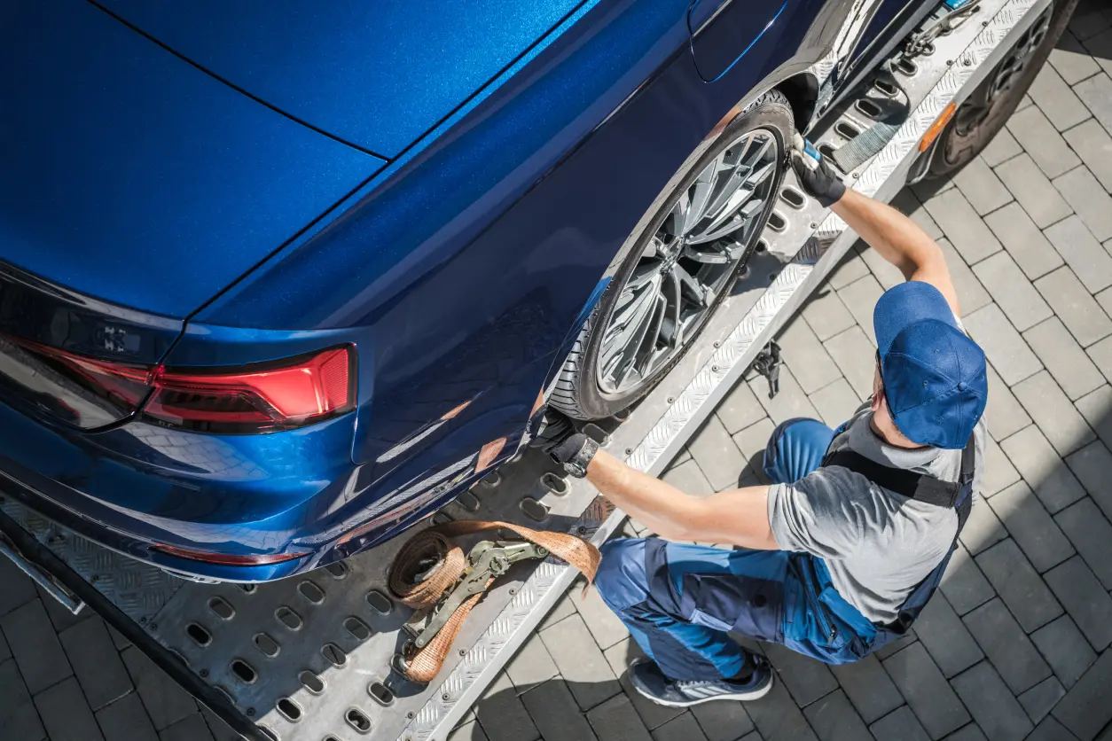 Mechanic securing blue car on tow truck.