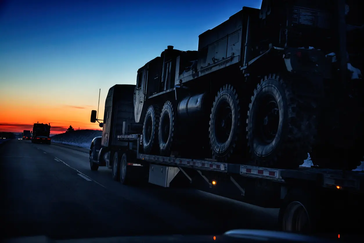 Military vehicles on a flatbed trailer at sunset.
