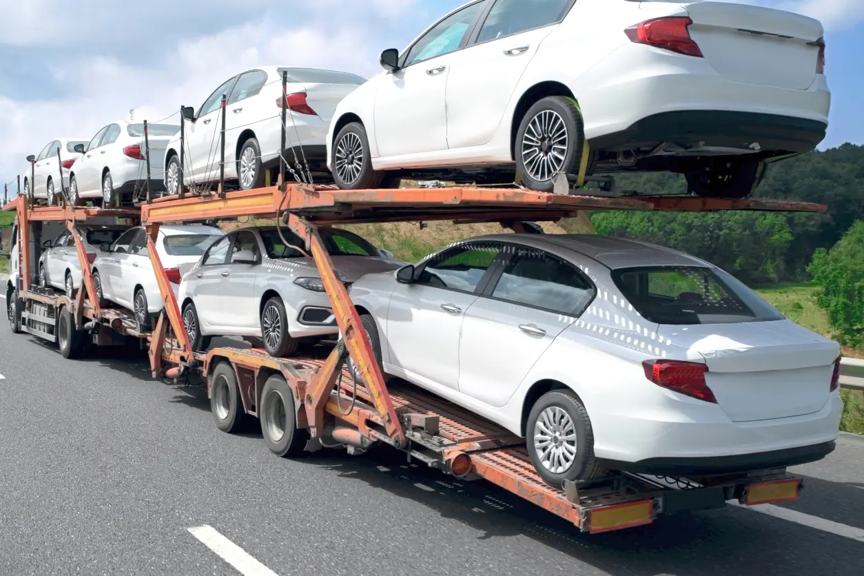 Car transporter carrying white sedans on highway.
